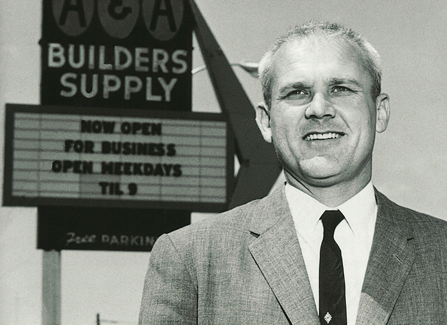 Black & White photo of Buzz Oates in a suite in front of A&A Builder's Supply sign